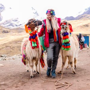 Alpaca adornada con pompones de colores frente a la montaña Vinicunca.